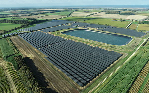 Aerial view of the Lightsource bp Thornham solar plant near Hunstanton, Norfolk — part of their UK Projects portfolio, with rows of panels installed across green fields beside a large reservoir.