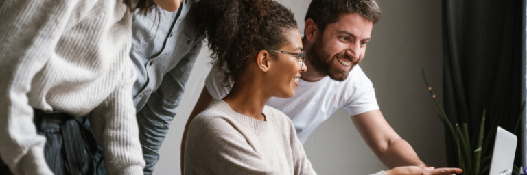 Three colleagues discussing over a computer in a well-lit office environment.