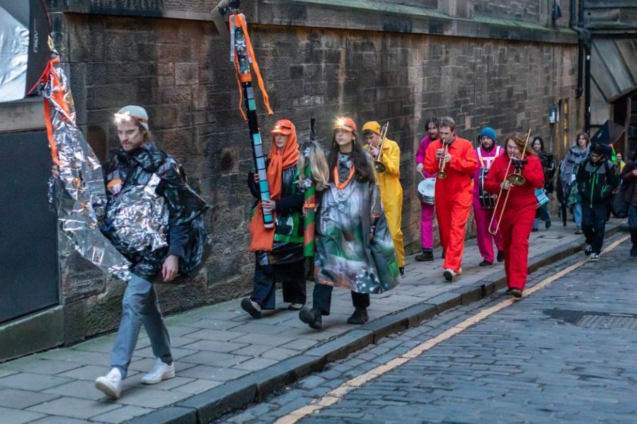 A group of people and a music band in colorful outfits walking in a procession.