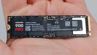 Close-up of a person's hand holding a Samsung 9100 Pro SSD with 4TB capacity. Text and QR codes are visible on the black surface.