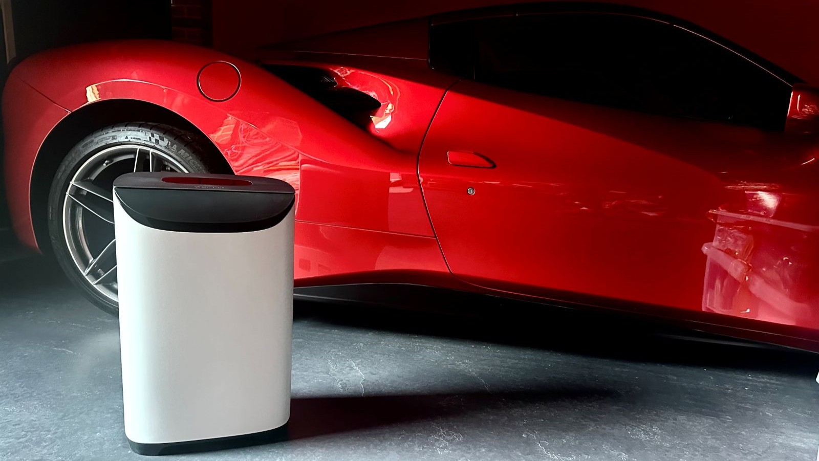 The Meaco DD8L dehumidifier in white on a concrete floor in a garage with a red super car behind it