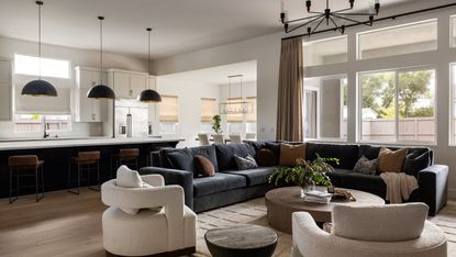 An open plan living room and kitchen space with a blue corner sofa, two curved accent chairs, and a neutral kitchen