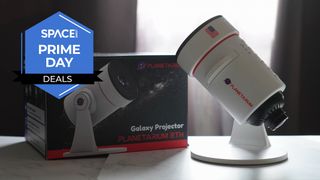 A Projector which looks like a microscope is placed on a white surface next to its black product box, with a window in the background.