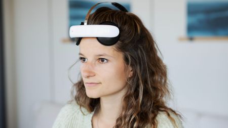 A woman is shown wearing the tDCS headset against a blurred background. The image is zoomed in so that only her head and shoulders are visible.