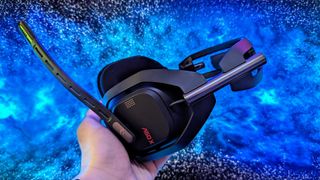 A person holds a black gaming headset with a prominent microphone against a vibrant blue and black galaxy-like background, creating a futuristic feel.