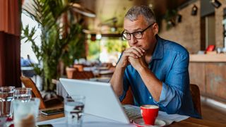 Mature man using laptop in a cafe, looking annoyed