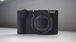Canon PowerShot V1 compact vlogging camera on a white desk, lens folded away
