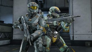 Two Spartan soldiers stand back-to-back in Halo Infinite, holding rifles inside a futuristic facility.
