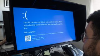 An office worker with a Blue Screen of Death error on a Windows PC.