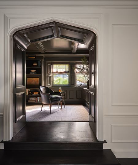 looking through an arched door to a panelled home office with a leather armchair on a white rug