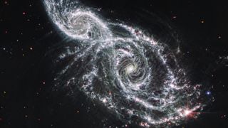 A deep space image showing the white gas and stars forming two spiral galaxies next to each other, stretching from the bottom right to top left of the image.