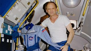 Astronaut Norman E. Thagard floats in the Space Shuttle Atlantis holding the flight suit he wore on Russia's Mir Space Station during the Mir-18 mission in 1995. This photo was taken on July 7, 1995, the last day of his four-month mission.