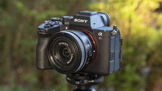 The Sony A7R VI camera with 24mm f/2.8 lens attached, it's mounted to a tripod outdoors, there's a natural background