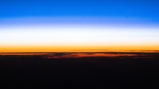 A sunset showing the black curve of the Earth with a golden band of light just above and a blue band of light above that