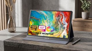 Portable KYY monitor displaying vibrant abstract art. Features include 1080p resolution, 15.6" screen, HDR, and 16:9 aspect ratio. Set on a wooden desk with a stylus and vase nearby.