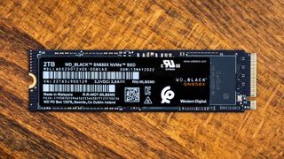 Close-up of a WD_BLACK 2TB SN850X NVMe SSD on a wooden surface. The sleek black rectangular device features labels and specifications in white text.