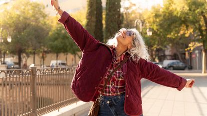 Senior woman standing with arms open wide and smiling, enjoying freedom