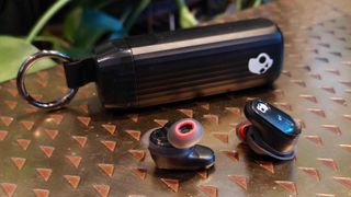 The Skullcandy Method 540 earbuds and carry case on a brown table.