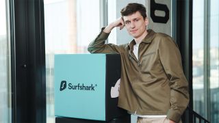 Surfshark CEO Dovydas Godelis posing in the company's offices next to a box displaying Surfshark's logo on a blue background