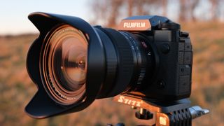A side on view of the Fujifilm X-H2 with the Fujifilm XF 16-55mm f/2.8 lens attached with a field in the background.