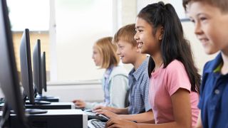 Smiling kids work at desktop computers