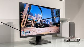 A sleek gaming monitor displays a vibrant cityscape from a video game. Next to it, a model car and speaker sit on a white desk, creating a modern tech vibe.
