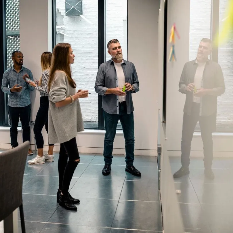 People standing in a workshop room looking at a sticky note wall