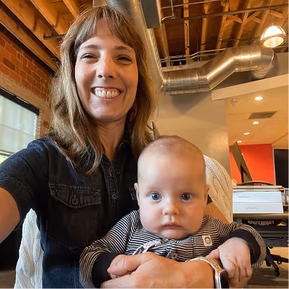 Atomic Object team member holding a baby in a modern office setting, embodying a culture of collaboration and support.