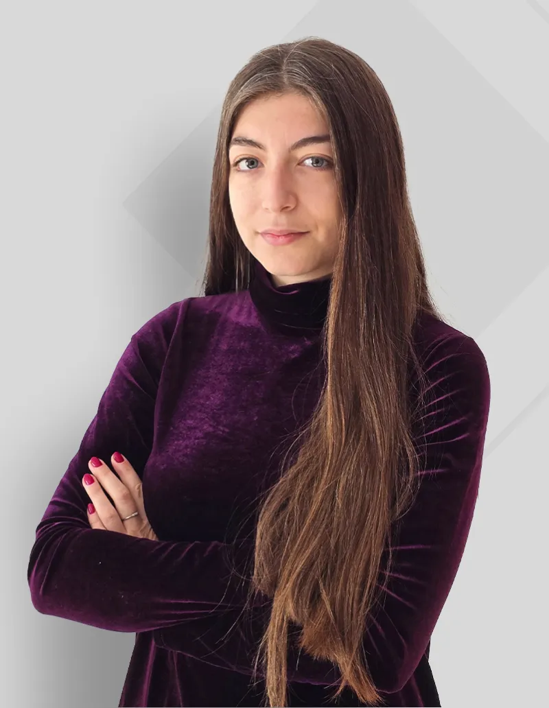 Confident woman with long brown hair wearing a purple velvet turtleneck, arms crossed.