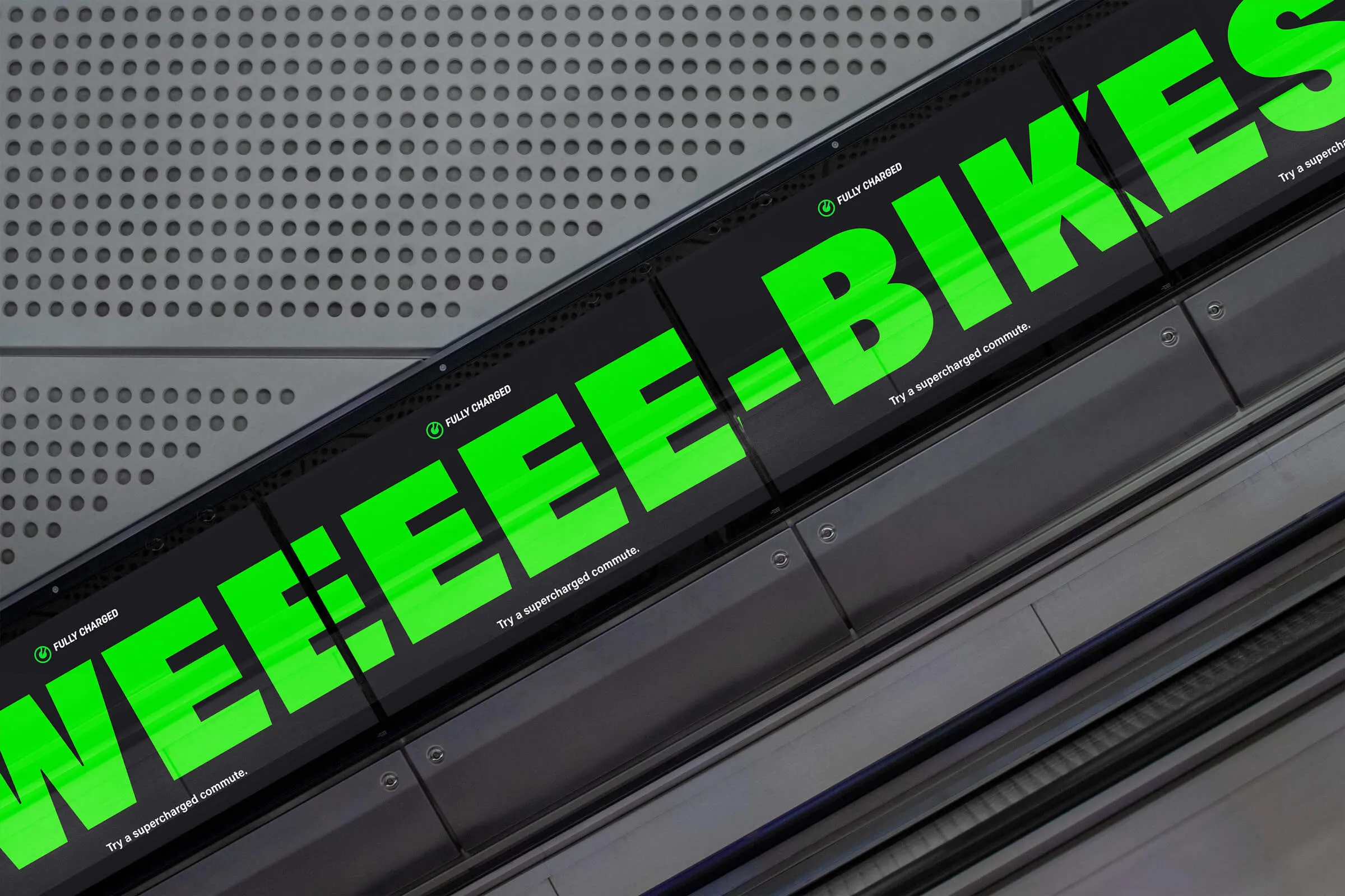 Ultrawide digital advert ascending up digital screens alongside an escalator, that reads 'WEEEEE-BIKES'