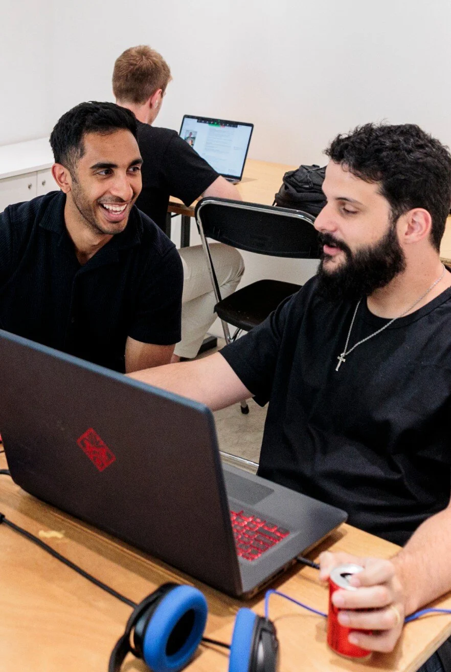 Two people sitting side by side at a table, collaborating while looking at a laptop screen.