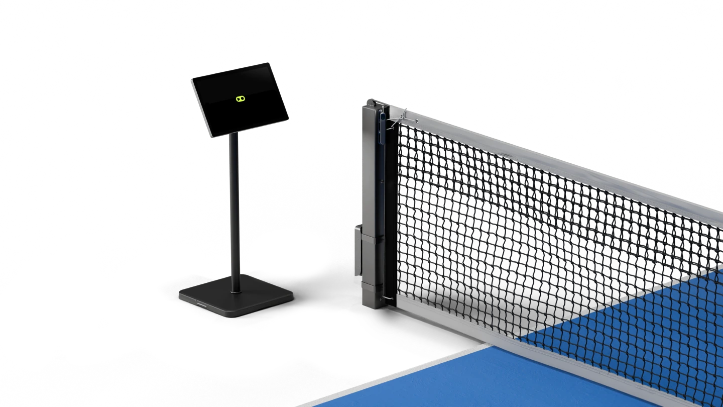 PlayReplay stand set up on a tennis court, featuring a mounted screen, processing unit, and camera attached to the net post, used for line calling and match analysis.