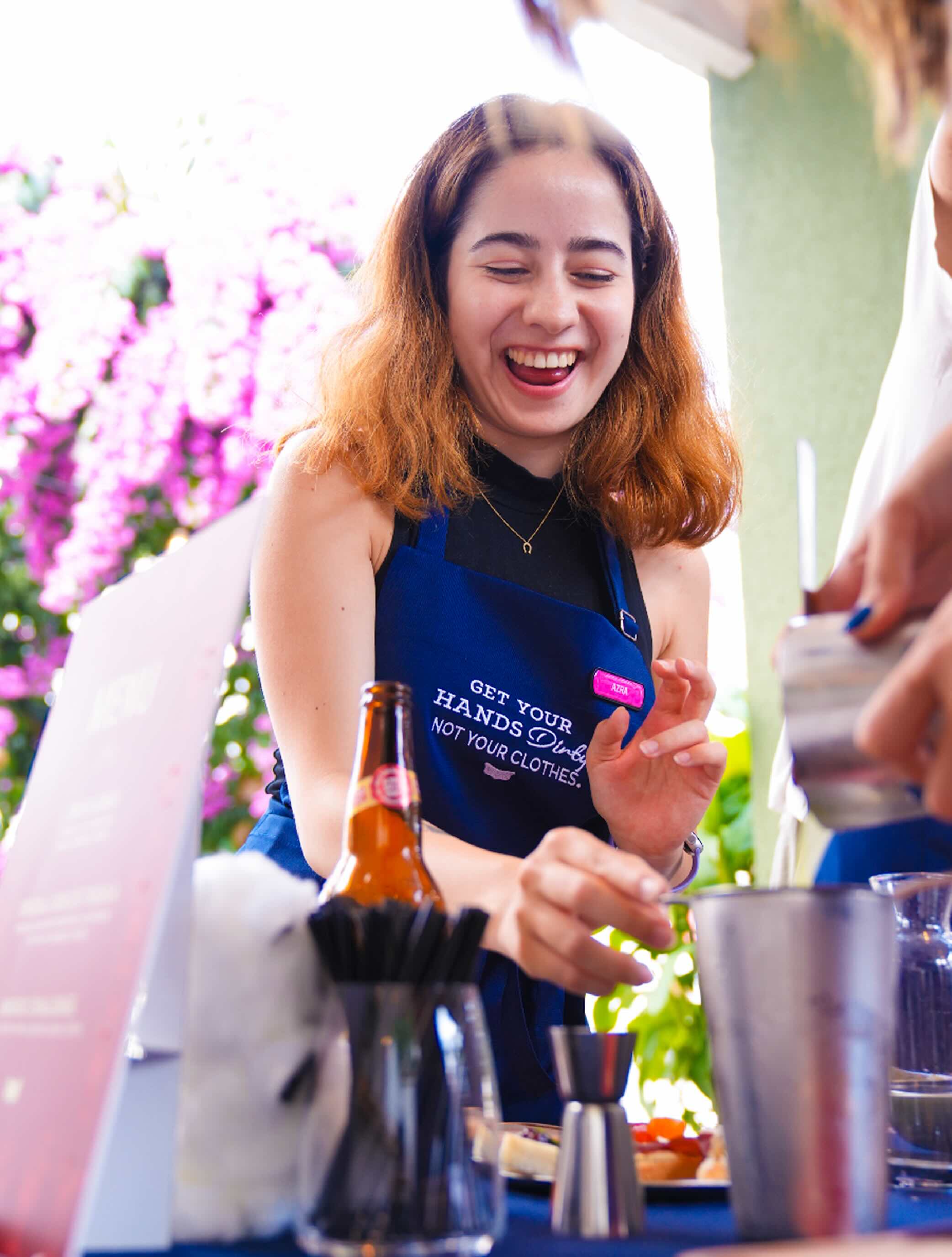 The girl is smiling as she prepares some beverage for another person.