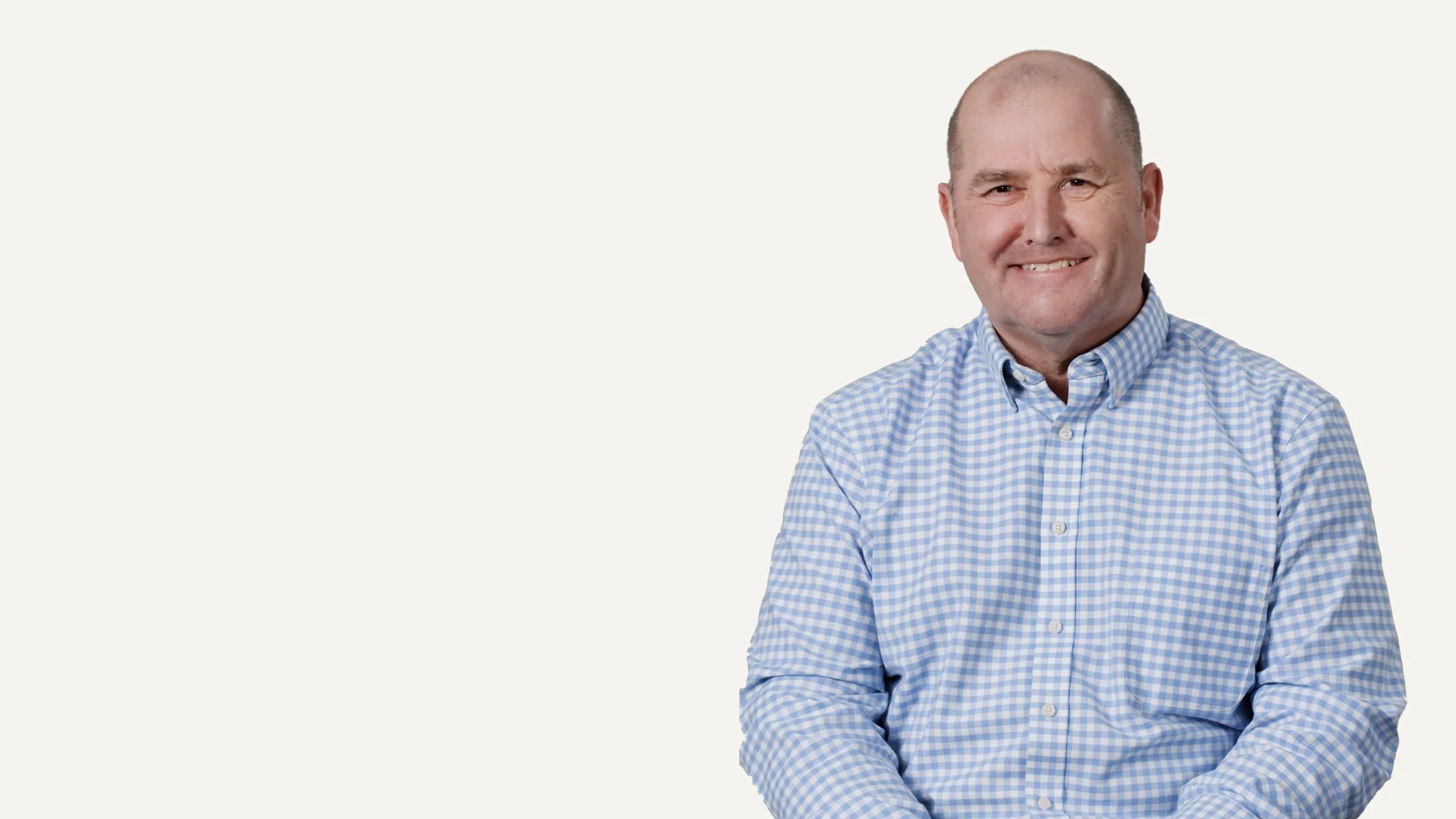 Bald man in blue gingham shirt smiling at the camera on white background.