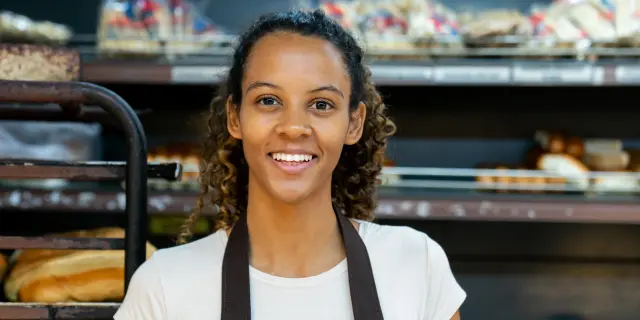 Smiling person standing in front of bakery shelves.