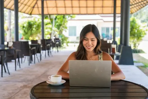 Woman smiling while working on a laptop at an outdoor café.