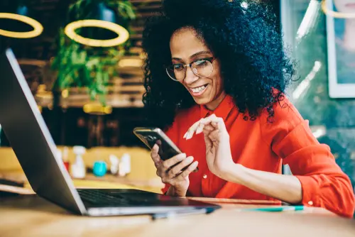 Woman smiling while using her phone next to an open laptop.