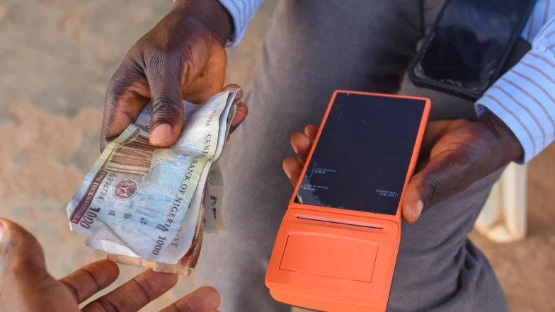 The hands of two people conducting a financial transaction with a point of sales POS terminal as Nigerian currency is exchanged.