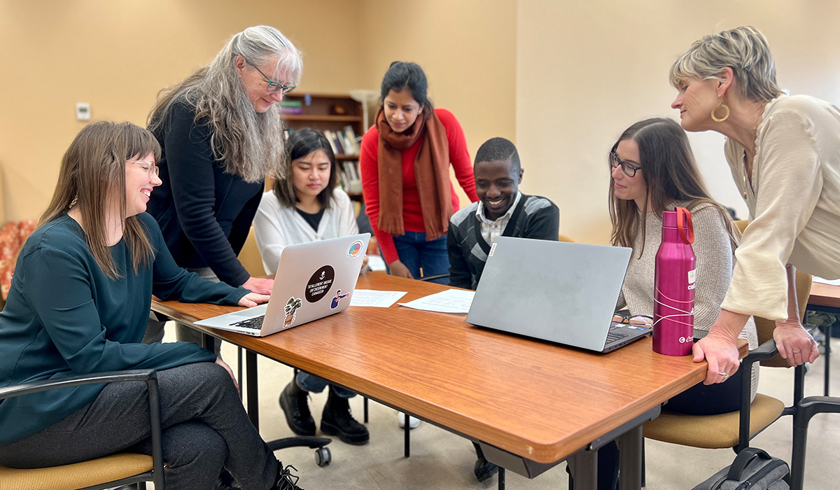 Students gathered around a laptop with a teacher.
