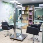 Современная парикмахерская с двумя черными креслами для укладки, стеклянными столами, зеркалами и полками со средствами для волос. В помещении деревянный пол, зеленые стены, цветочная фреска на стене. Детали для наших контактов предоставляются по запросу. Современная парикмахерская с двумя черными креслами для укладки, стеклянными столами, зеркалами и полками со средствами для волос. В помещении деревянный пол, зеленые стены, цветочная фреска на стене. Детали для наших контактов предоставляются по запросу.