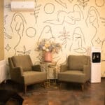 Два оливково-зеленых кресла стоят у небольшого стеклянного столика с вазой с засушенными цветами на фоне светлой стены, украшенной абстрактным линеарным искусством. Уютная комната, где наши контакты легко доступны, с диспенсером для воды и кондиционером. Два оливково-зеленых кресла стоят у небольшого стеклянного столика с вазой с засушенными цветами на фоне светлой стены, украшенной абстрактным линеарным искусством. Уютная комната, где наши контакты легко доступны, с диспенсером для воды и кондиционером.