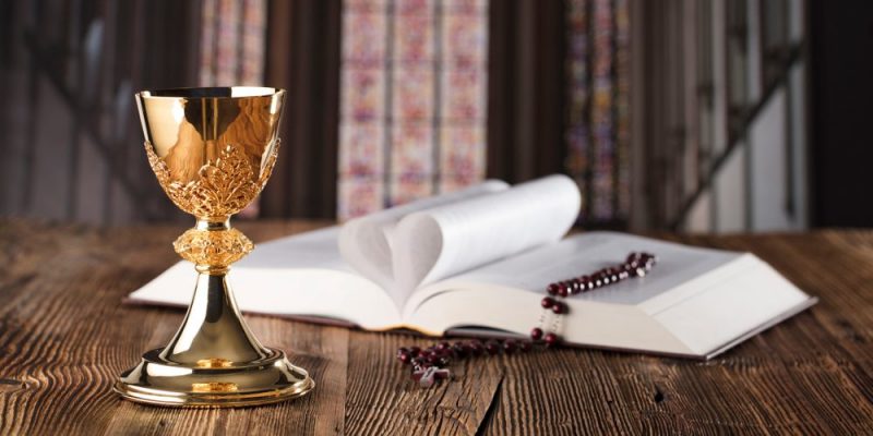 Biblia abierta junto a un rosario y un cáliz