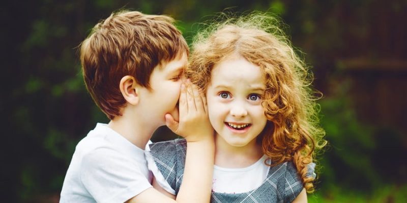 Un niño le dice un secreto a una niña.