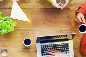 A group of people collaborating around a wooden table. There are coffee cups and a laptop on the table.