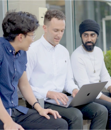 Three men collaborating on a laptop in an outdoor workspace