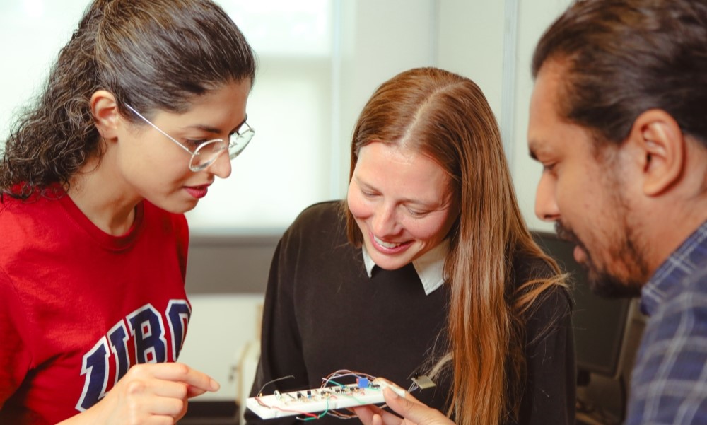Grad students examine a circuit board.