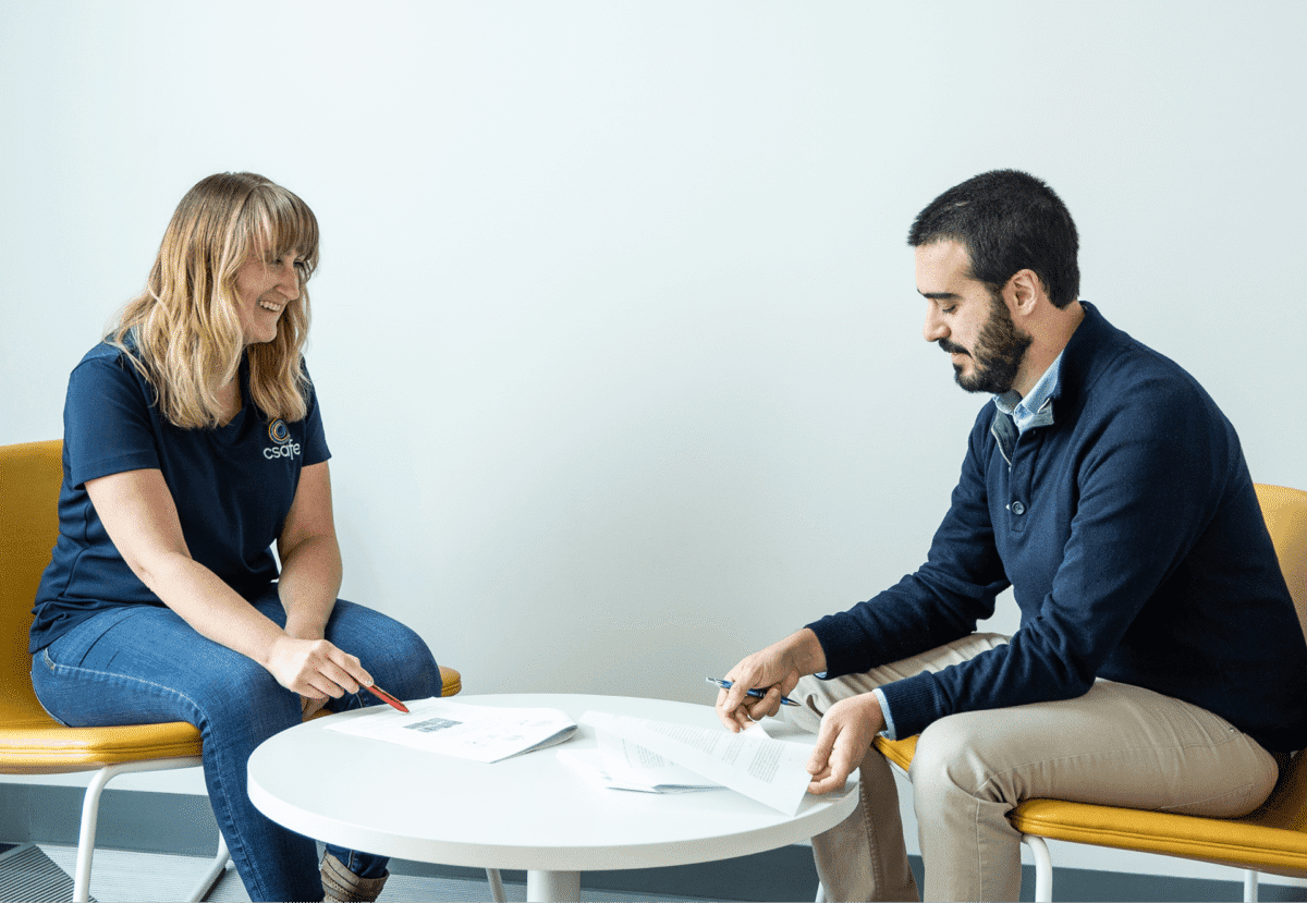 Two people sitting at a round table discussing documents and smiling in a bright, modern office setting.