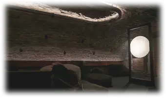 Salle voûtée en pierre avec installation lumineuse circulaire au plafond et un grand disque lumineux au sol, créant un espace d’écoute immersif.