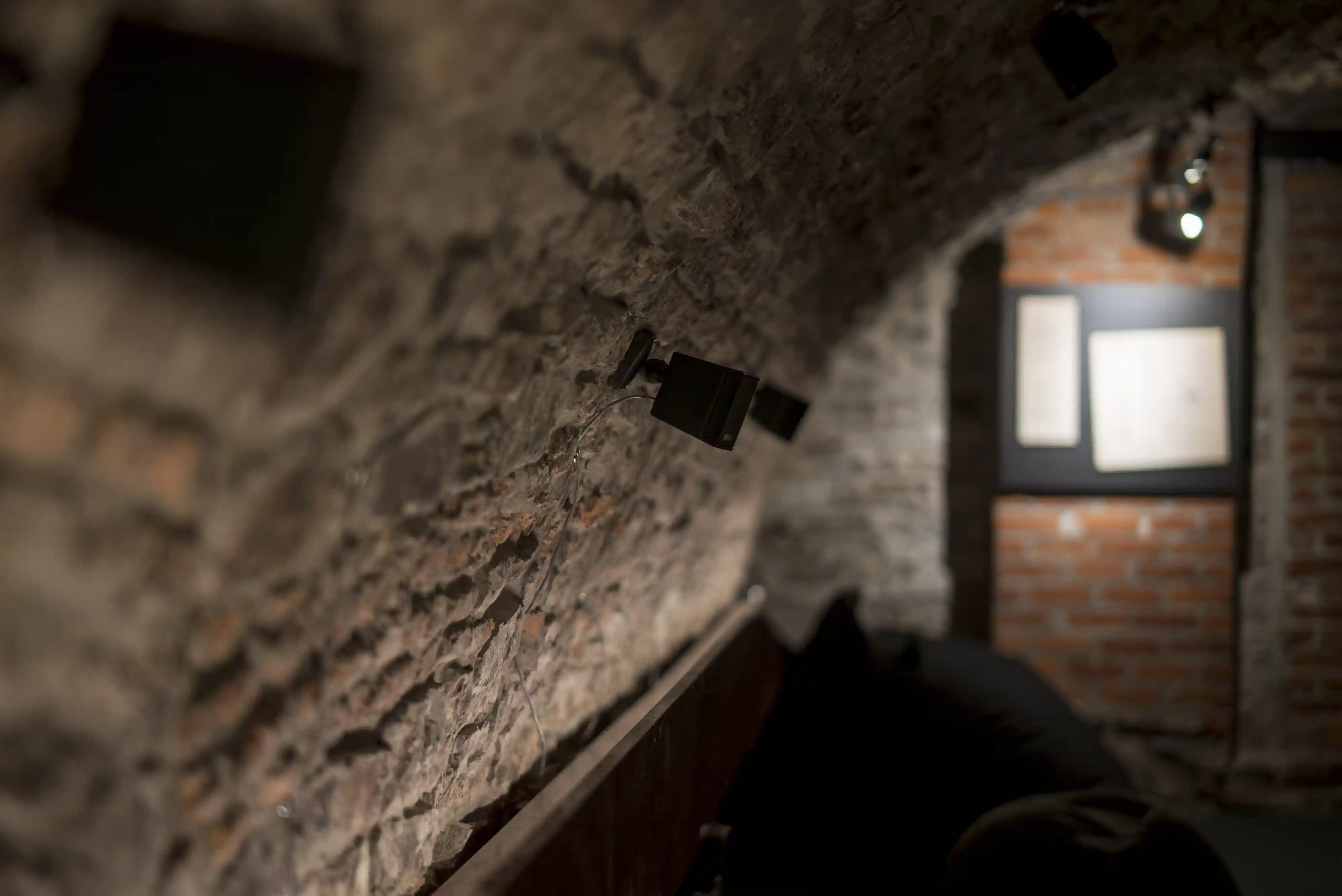 Gros plan sur un mur de pierre voûté équipé de petits haut-parleurs orientés vers une installation immersive.