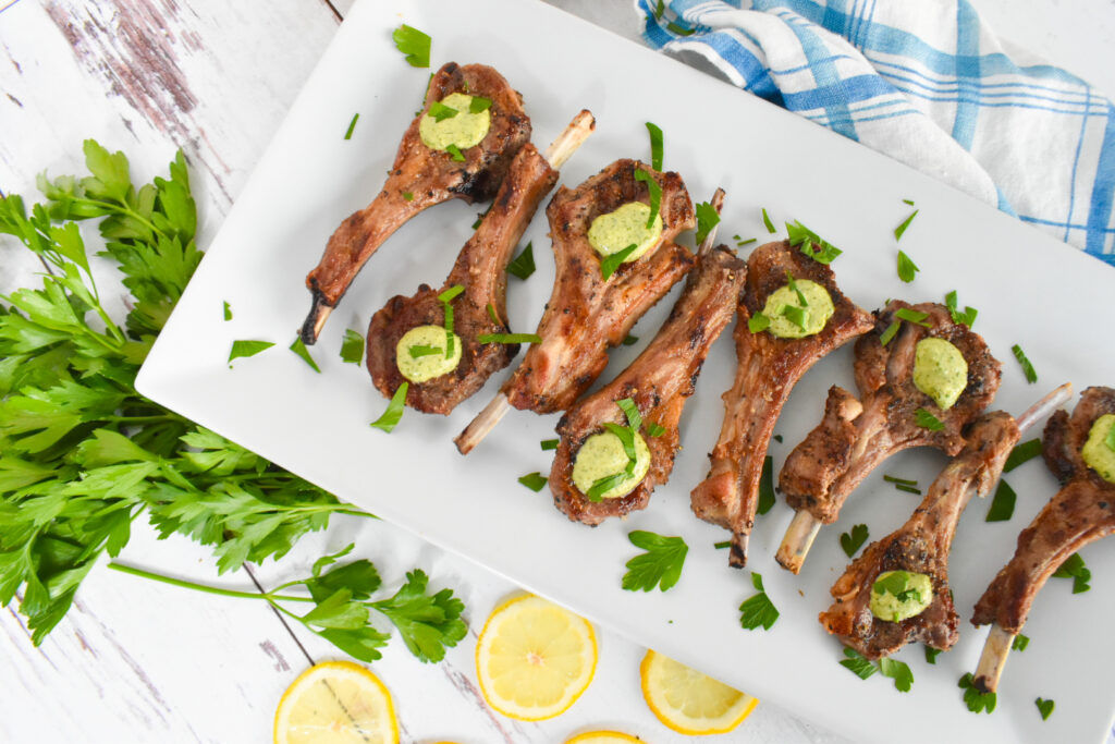 lamb rib chops on white plate with lemon mint gremoloata garnished on top and parsley and lemon slice garnish